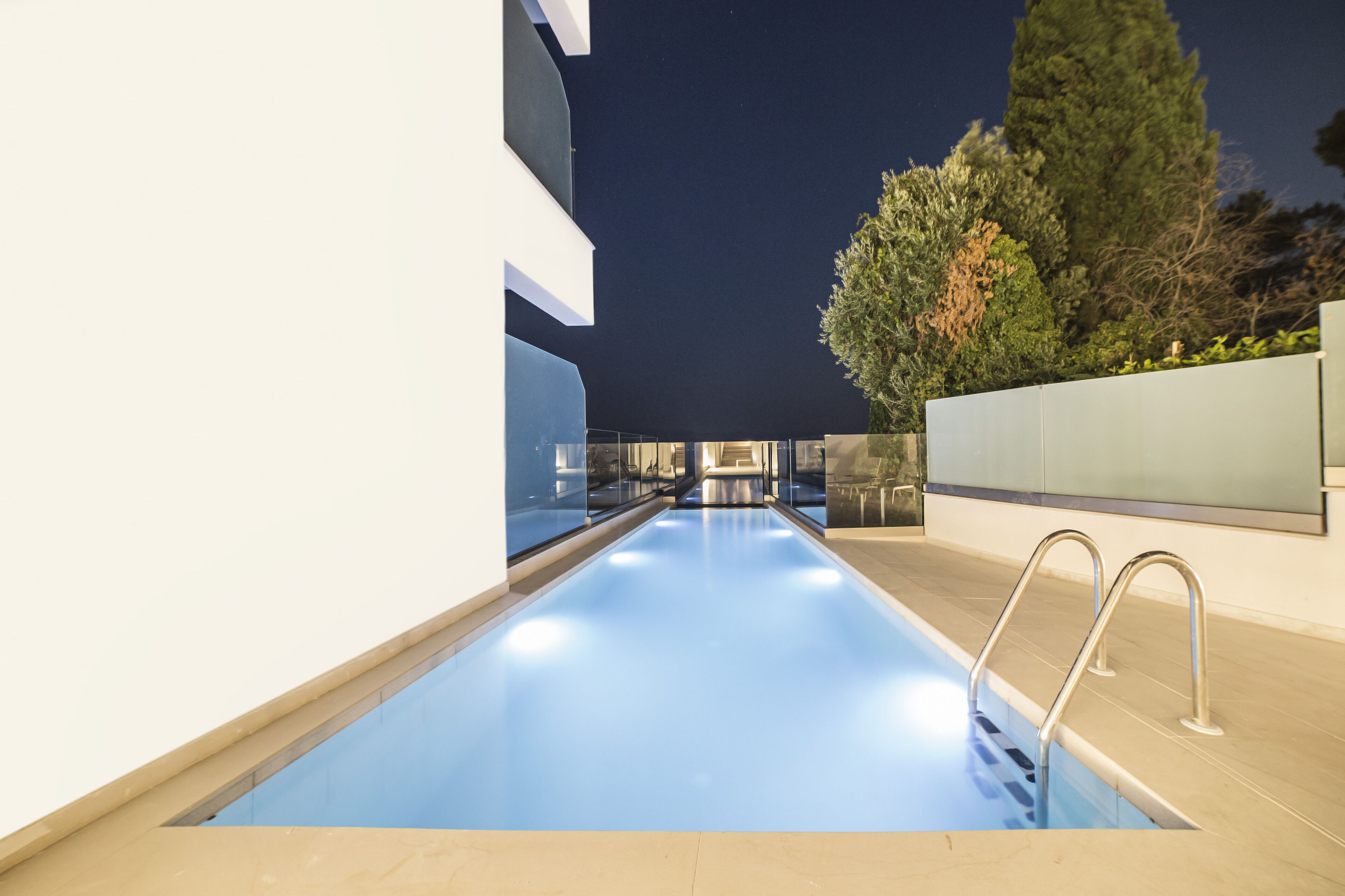 Una piscina coberta moderna amb parets de vidre transparent, aigua blava i una escala metàl·lica.