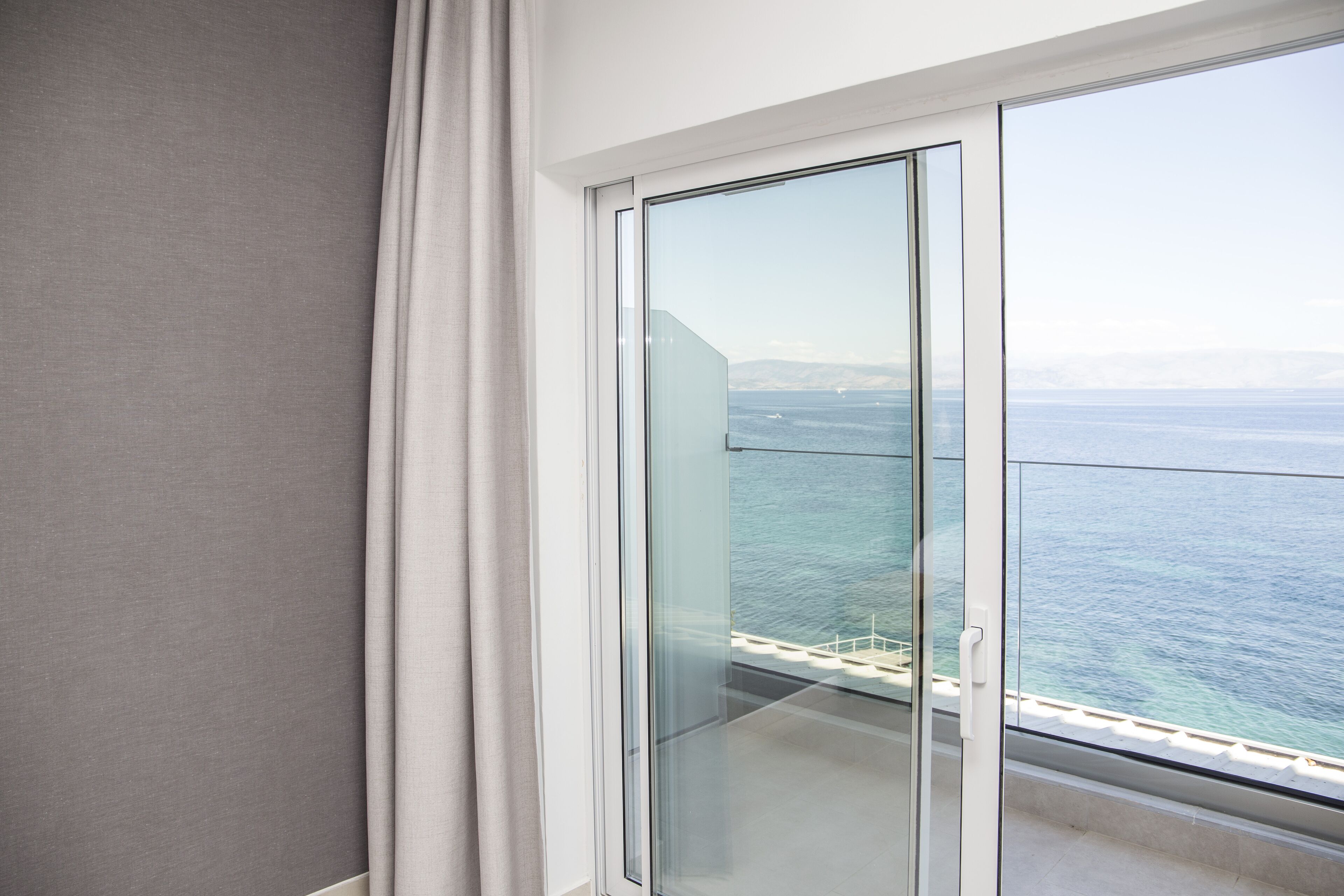 A balcony with a glass door overlooking the sea.