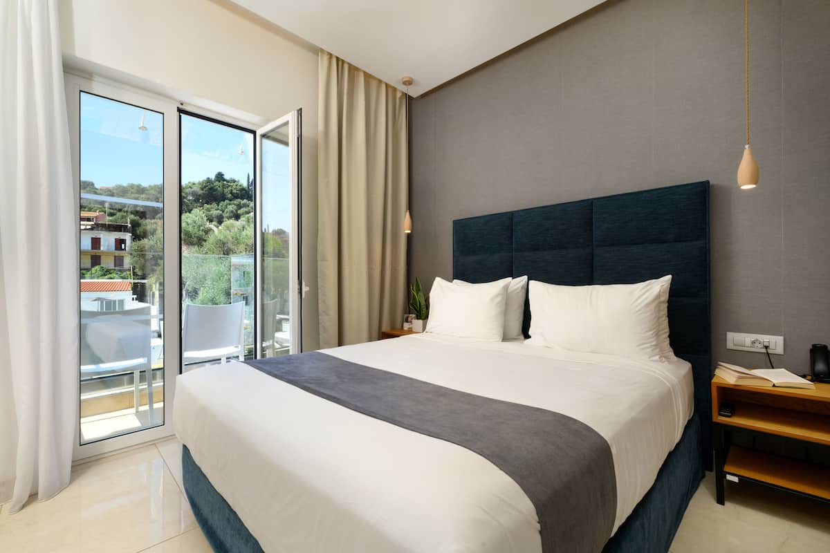 Habitación de hotel moderna con una cama grande, una mesita de noche y vistas al exterior a través de una puerta corrediza de vidrio.