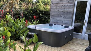 Ein Whirlpool auf einer Holzterrasse, umgeben von viel Grün.