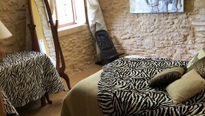 Ein Schlafzimmer mit einem Bettbezug mit Zeprazermuster, einem Holzstuhl, einem Spiegel und einer an der Wand befestigten Elefantsskulptur.