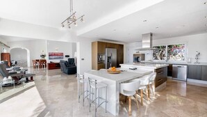 A modern kitchen with a large island, stainless steel appliances, and a dining area with white chairs. - Villa Catalina (Benalmádena)
