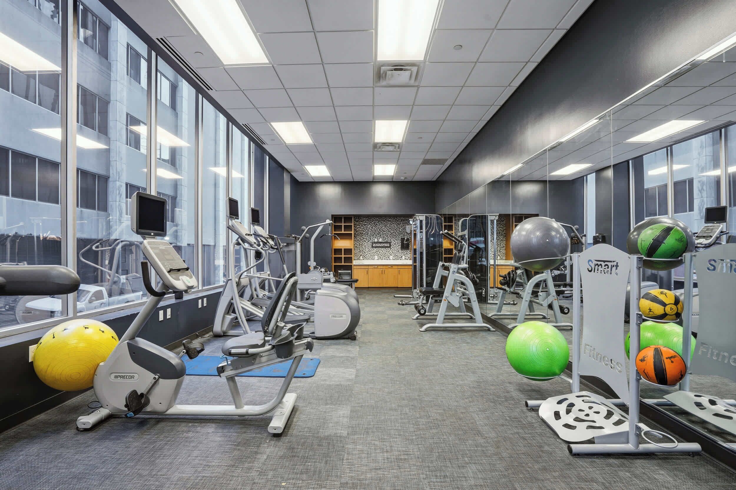 A gym with exercise equipment, a mirrored wall, and large windows.