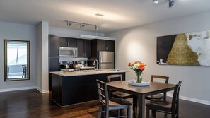 A modern kitchen with dark cabinetry, stainless steel appliances, and a central island. - CozySuites - Remi (Dallas)