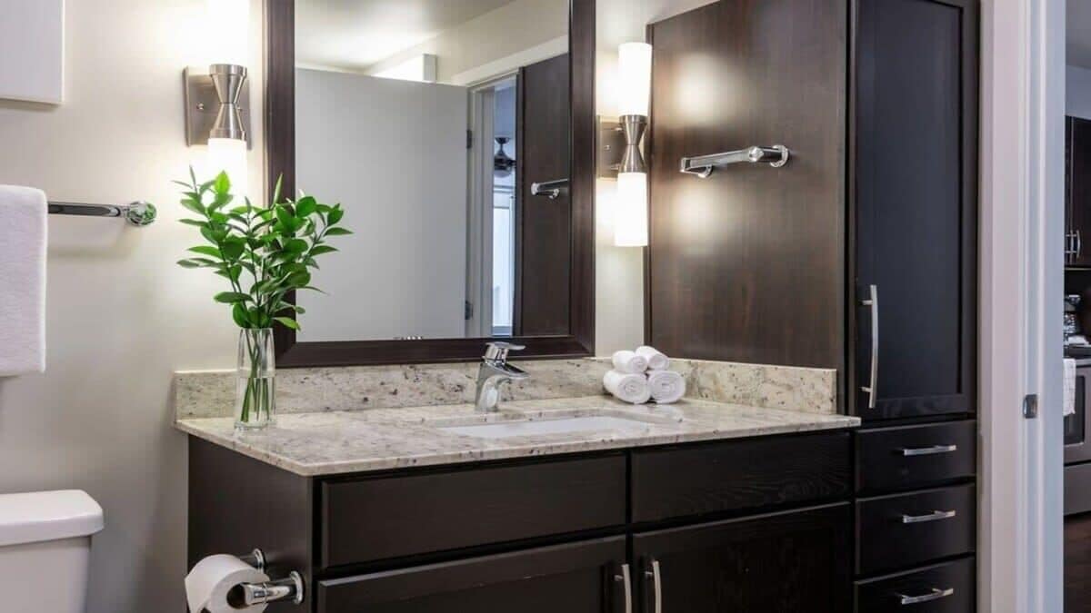 A modern bathroom with a marble sink, dark cabinetry, a large mirror, and a towel rack.