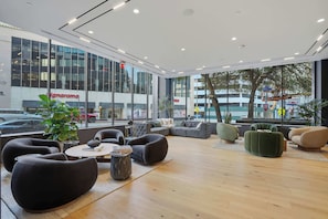 A modern interior with a seating area, large windows, and a view of the street outside. - CozySuites - Remi (Dallas)