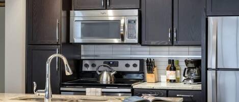 A modern kitchen with dark cabinetry, stainless steel appliances, and a marble countertop.