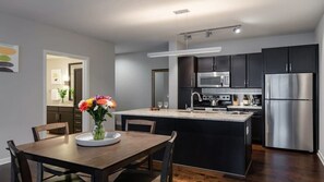 A modern kitchen with dark cabinets, stainless steel appliances, and a central island. - CozySuites - Remi (Dallas)