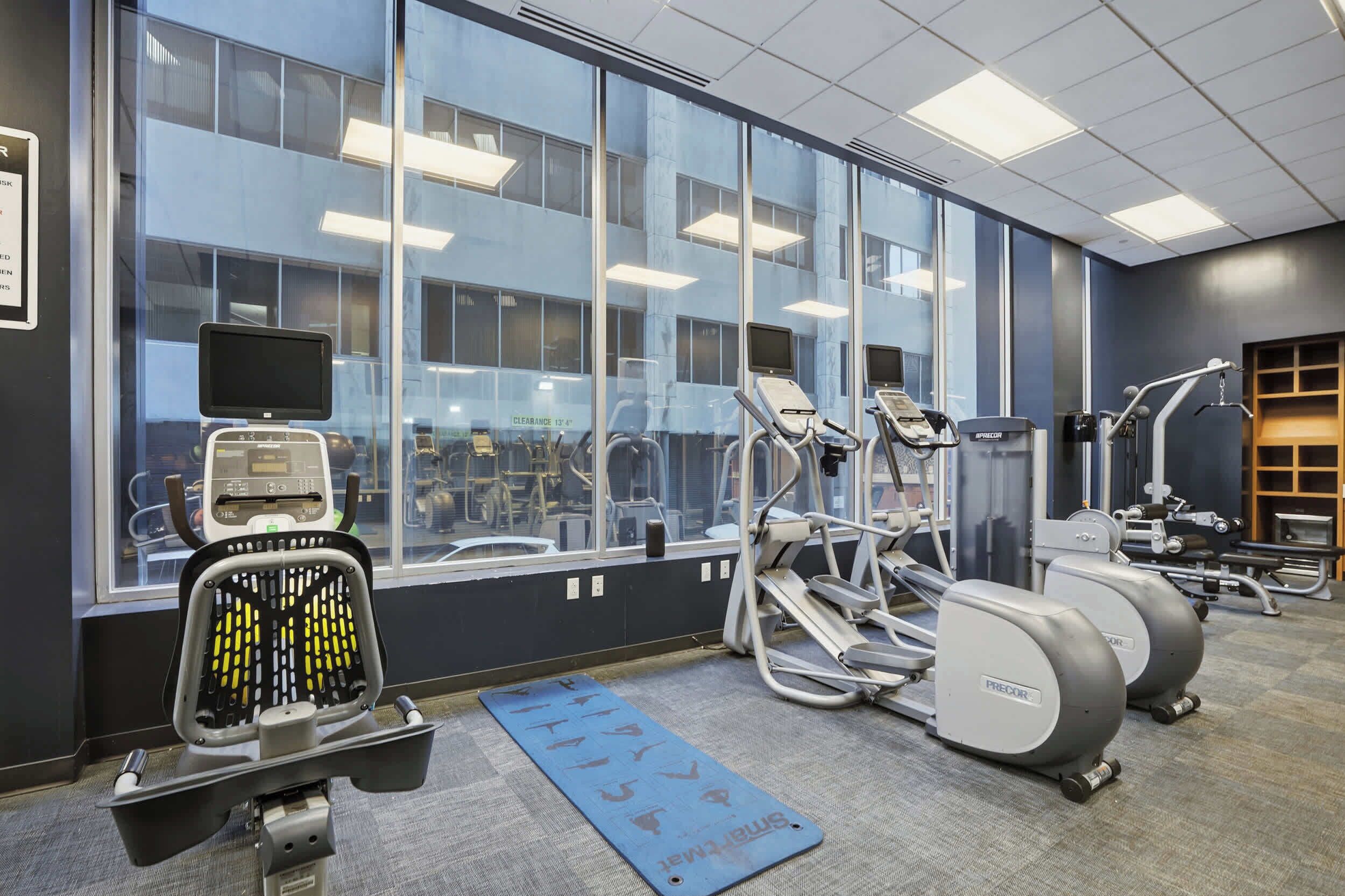 Een fitnessruimte met cardioapparaten, een hometrainer en een blauwe mat op de vloer.
