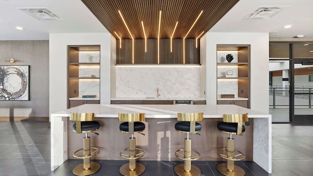 A modern kitchen with a central island, bar stools, and built-in shelves. - CozySuites - Remi (Dallas)