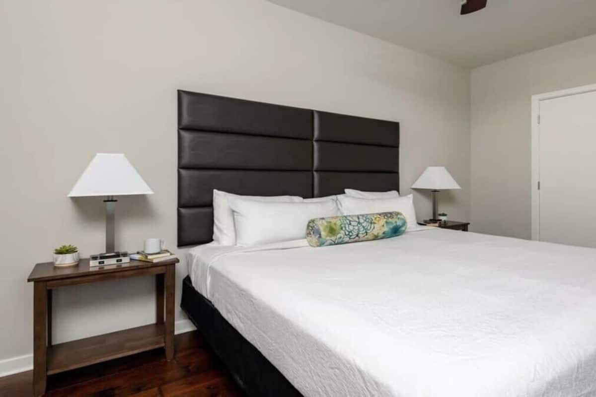 A hotel room with a large bed, two bedside tables with lamps, a white door, and a dark headboard.