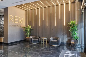 A modern reception area with a polished black marble floor, two grey armchairs, a small round table, and a potted plant. - CozySuites - Remi (Dallas)