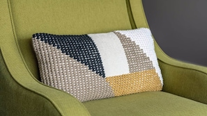 A green upholstered chair with a textured, geometric-patterned pillow. - CozySuites - Remi (Dallas)