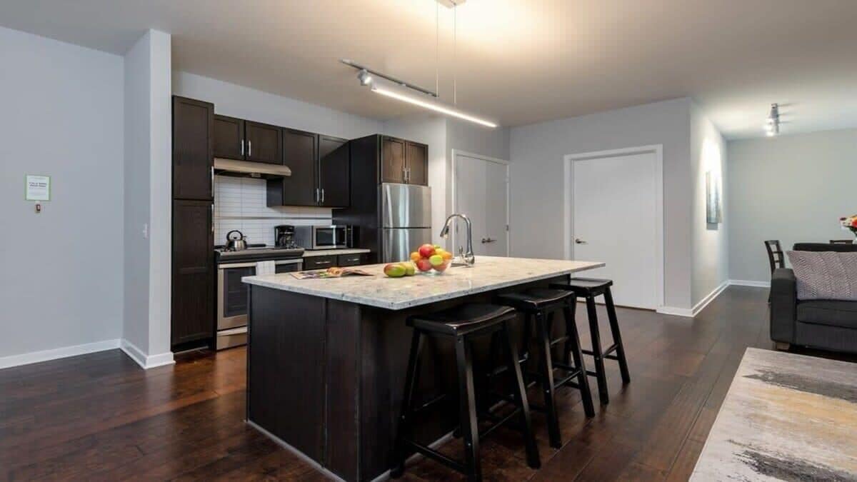 A modern kitchen with dark wood cabinets, stainless steel appliances, and a central island with stools.