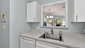 A kitchen with a granite countertop, stainless steel sink, white cabinets, and a large mirror above the sink. - 2br/2ba Walk to pier/village area.  1/2 mile to beach (Saint Simons Island)