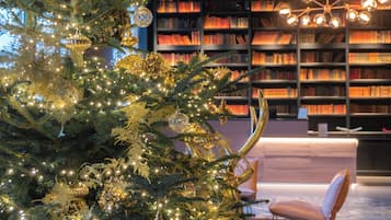 Et juletræ med lys og pynt i et rum med en bogreol og en moderne stol.