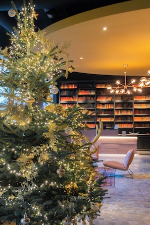 A Christmas tree with lights and ornaments in a room with a bookshelf and a modern chair. - Hôtel LÉONOR the place to live By Stay Collection (Strasbourg)