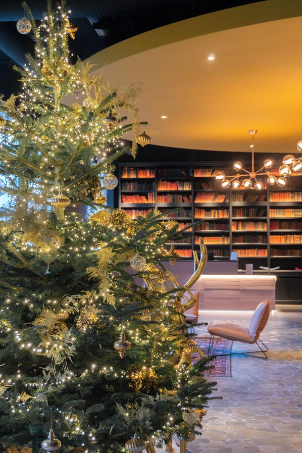 A Christmas tree with lights and ornaments in a room with a bookshelf and a modern chair. - Hôtel LÉONOR the place to live By Stay Collection (Strasbourg)