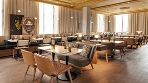 Un'ampia sala da pranzo con diversi tavoli e sedie, grandi finestre con tende e un lampadario.