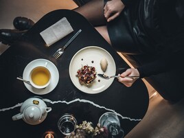 A table with a teapot, cups, a plate with dessert, and a fork.