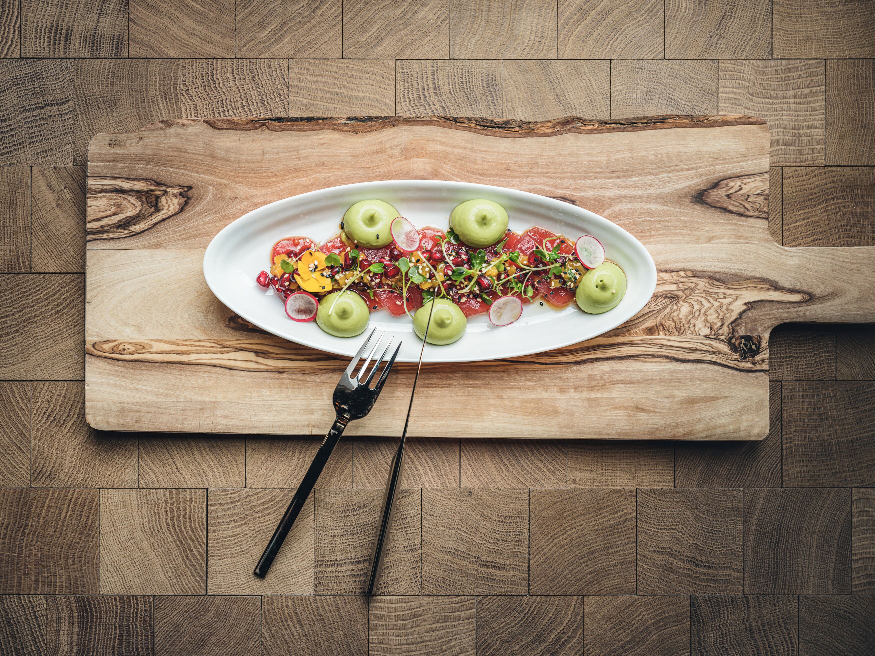 Une table en bois sur laquelle se trouve une assiette ovale blanche contenant une salade, une fourchette et une planche à découper en bois.