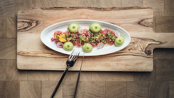 Een houten tafel met een wit, ovaal bord met een salade, een vork en een houten snijplank.
