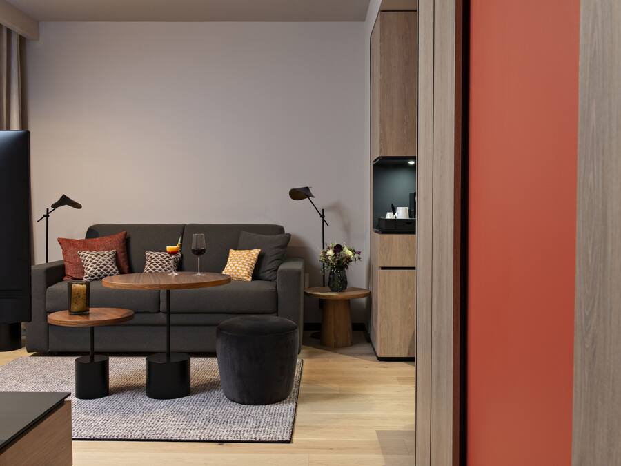 Ein modernes Wohnzimmer mit einem grauen Sofa, zwei Beistelltischen, einem Couchtisch und einem schwarzen Ottomanen.