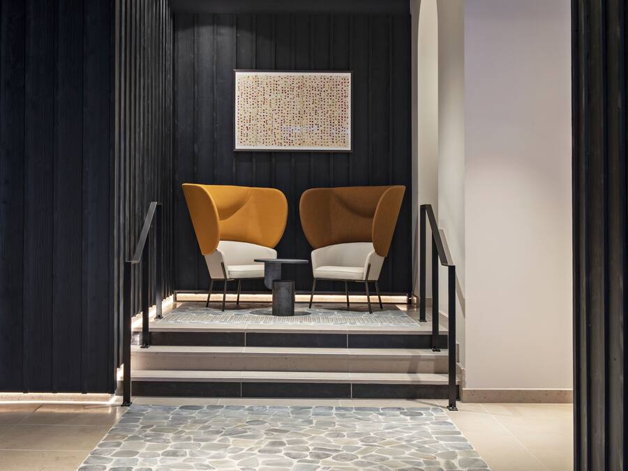 Een moderne lobby met een trap naar een hoger niveau, met twee fauteuils en een bijzettafeltje.