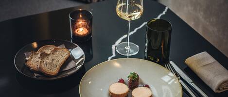 A dining table with a plate of food, a glass of white wine, and a candle.