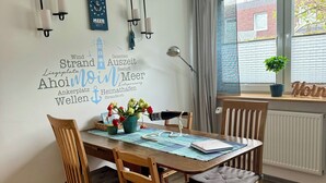A dining area with a wooden table, four chairs, a potted plant, and a wall with a decorative sign. - Maritime vacation apartment in Wilhelmshaven on the North Sea (Wilhelmshaven)