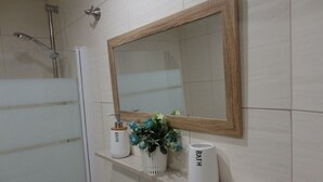 Une salle de bain avec un grand miroir, une douche et deux vases blancs sur lesquels est inscrit le mot « BATH ».