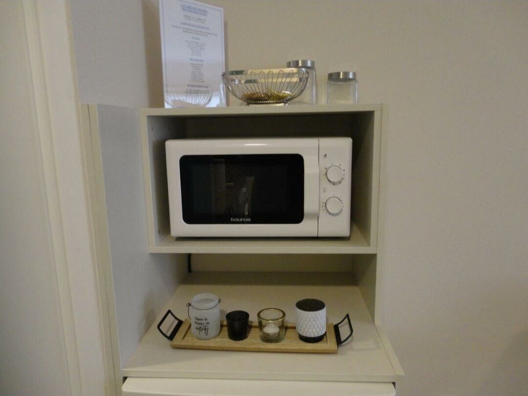 Een witte magnetron op een plank met eronder een dienblad met een mok, een kaars en een klein bakje.