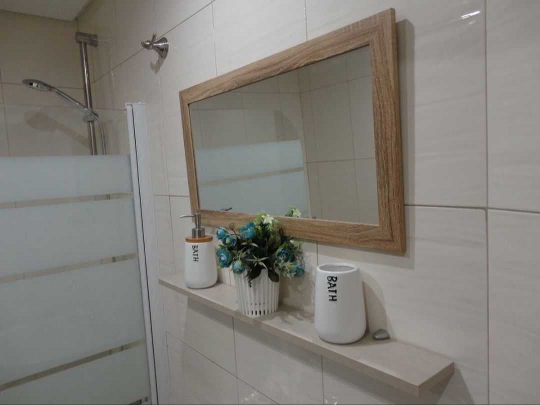 Un baño con un espejo grande, una ducha y dos jarrones blancos con la palabra "BATH" en ellos.