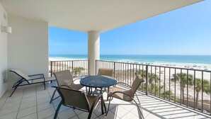 A balcony with a table and chairs, overlooking a beach with umbrellas and the ocean. - 3rd Floor!! New Owner, New to the Rental Market, Lazy River and Slide!! (Orange Beach)