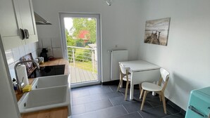 Cocina compacta con un lavamanos, comedor con mesa y sillas, ventilador de techo y vista a un espacio exterior por medio de una puerta de vidrio.