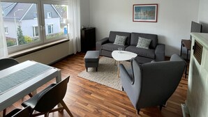 Una sala de estar moderna con sofá, reposapiés, mesa de centro y un comedor con mesa y sillas.