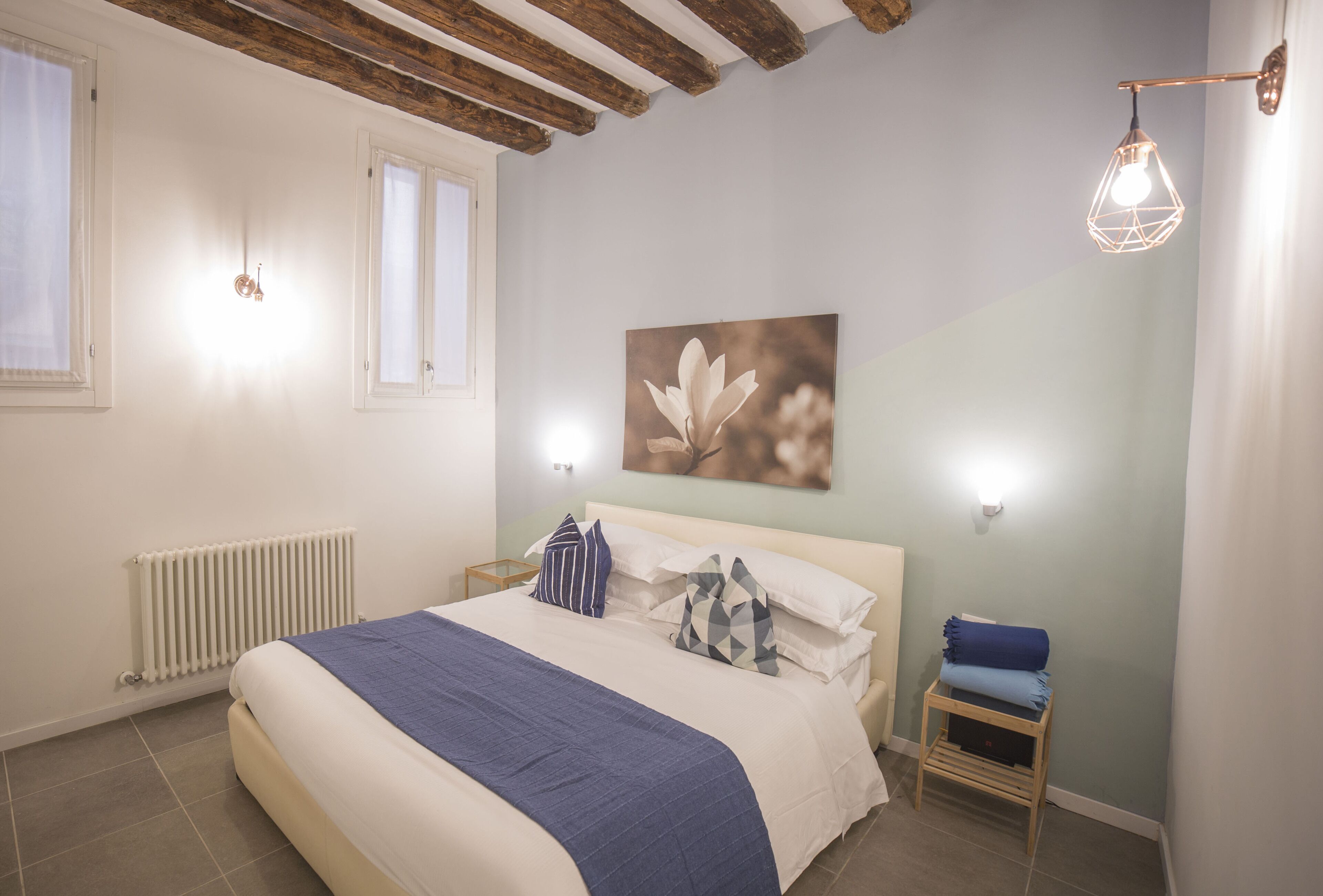 Ein Schlafzimmer mit Bett, Heizkörper, Nachttisch, Wandleuchte und Fenster.