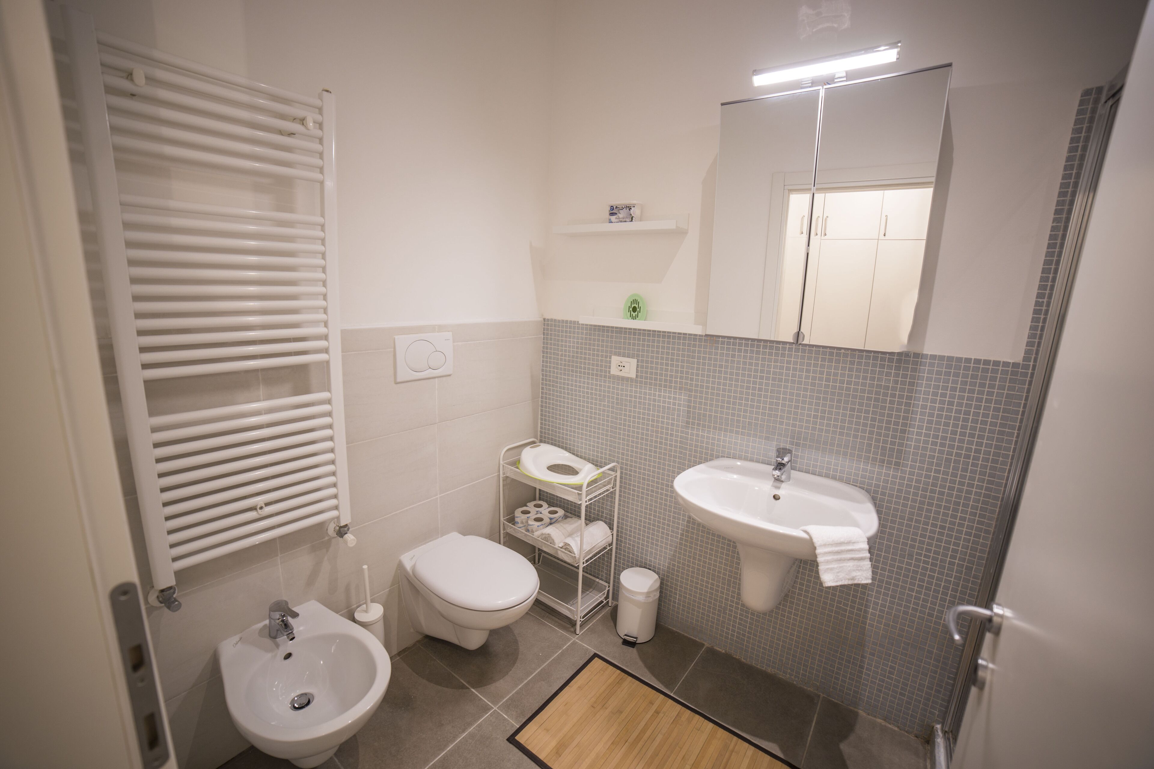 A modern bathroom with a toilet, bidet, sink, and towel rack.
