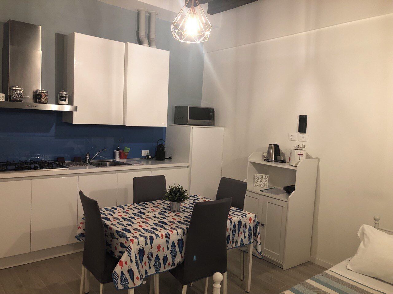A compact kitchen with white cabinets, a microwave, and a dining area with a patterned tablecloth.