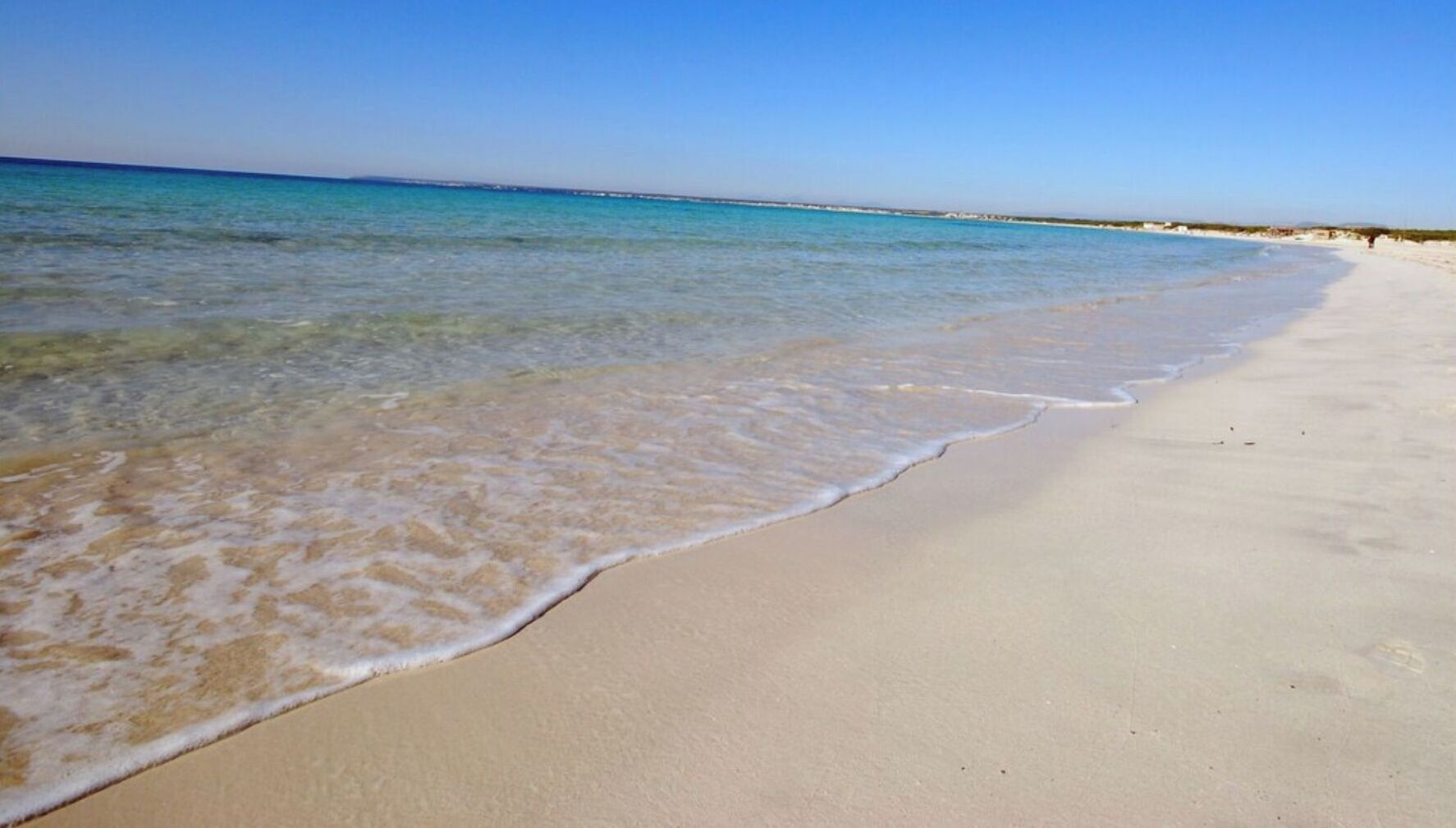 A beach with clear blue water and a sandy shore.