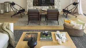 A living room with a stone fireplace, a television, and a seating area with two chairs and a table.