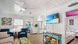 A spacious living room with a large TV, a sofa, a coffee table, and a dining area. - Sassy Seagull -Classic beach cottage, moments from the sand, beautiful pool! (Anna Maria)