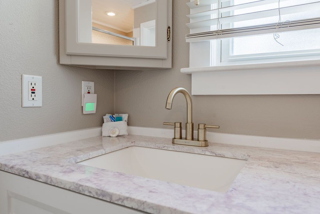 A bathroom with a marble sink, a gold faucet, a mirror, and a window with blinds.