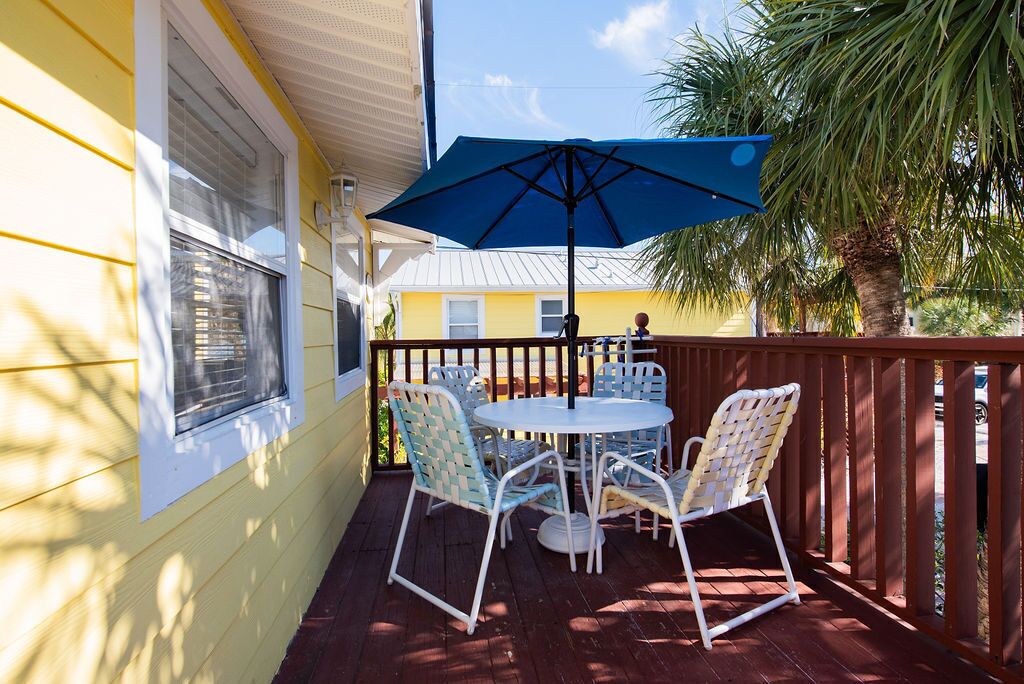 A covered patio with a table and chairs, a blue umbrella, and a wooden fence.