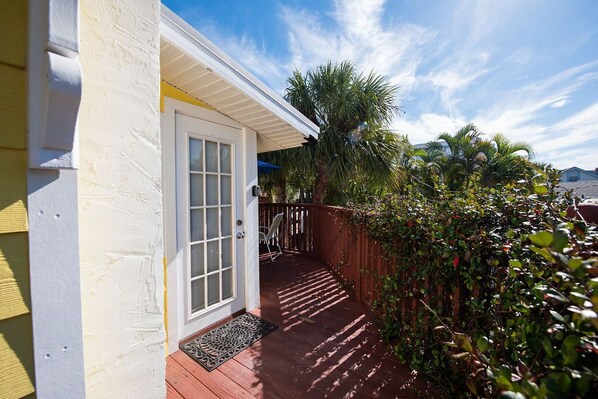 A covered porch with a wooden deck, a white door with glass panels, and a metal doormat.