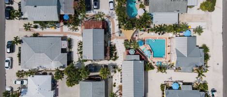 An aerial view of a residential area with multiple houses, a swimming pool, and parked cars.