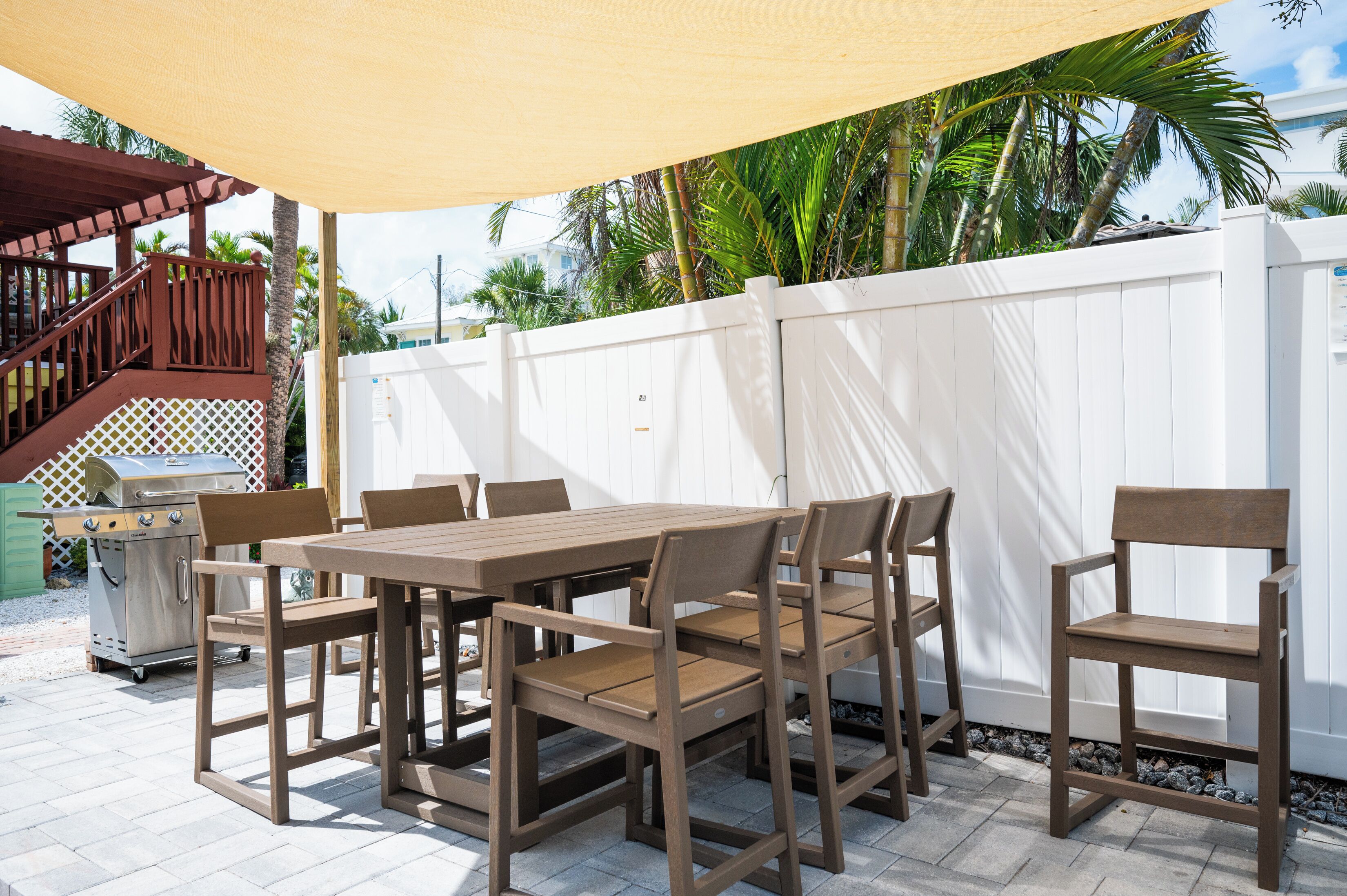 An outdoor patio with a wooden table and chairs, a barbecue grill, and a white fence.