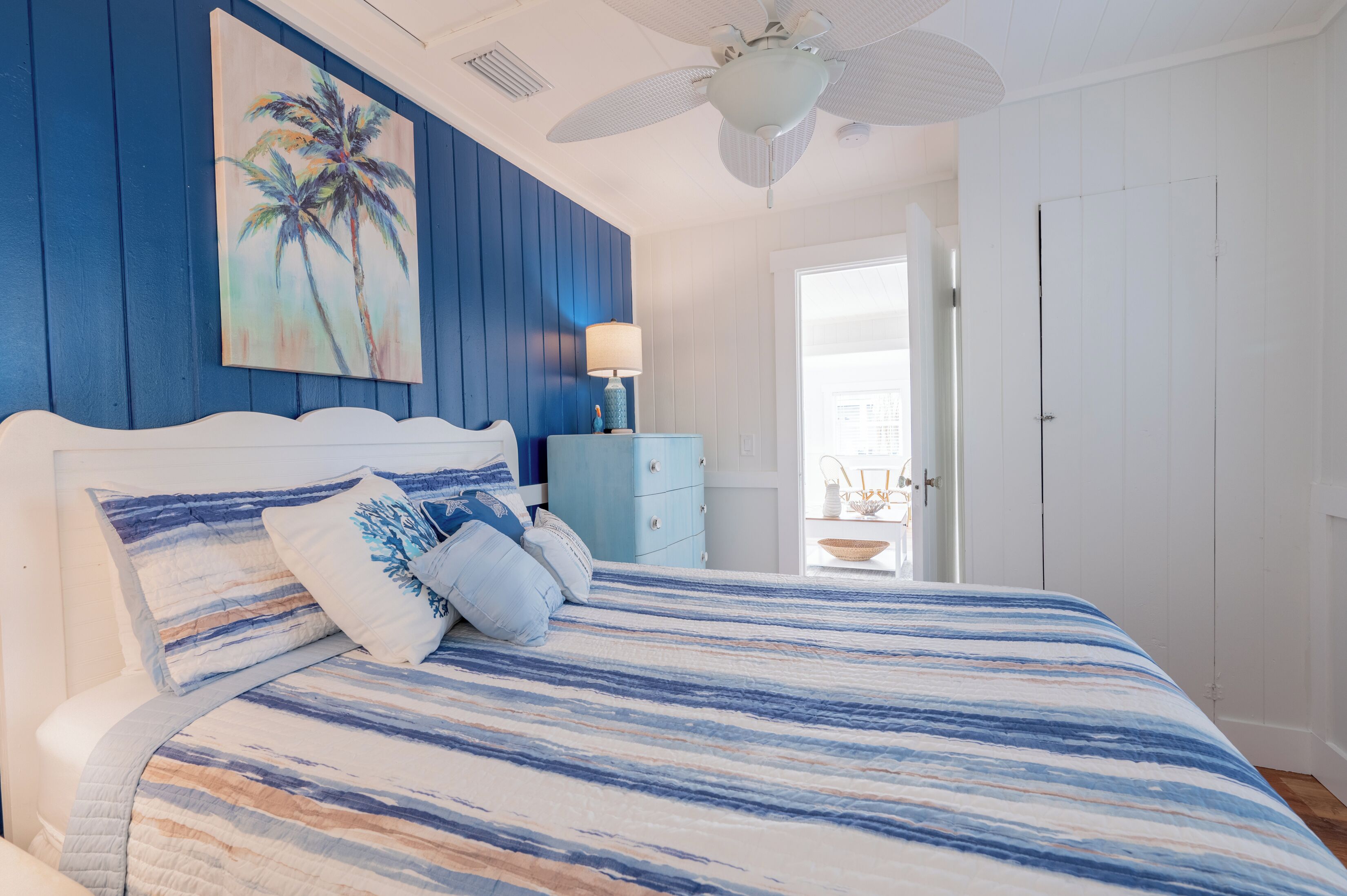 A bedroom with a bed, a nightstand, a painting, and a door leading to another room.