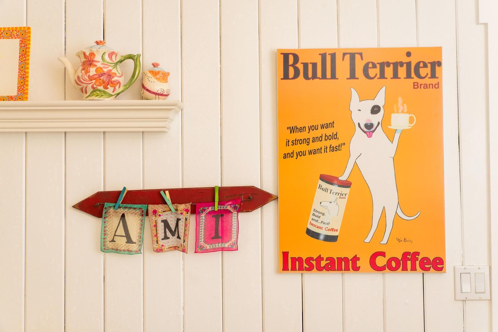 A wall with a framed poster of a dog holding a coffee cup, a shelf with decorative items, and a clothespin display with letters.