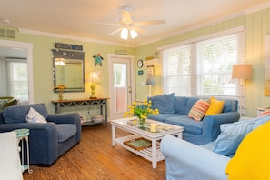 A cozy living room with a blue sofa, a coffee table, and a ceiling fan. - Anna Maria Beach Cottage 110  Traditional beach cottage, moments from the sand! (Anna Maria)